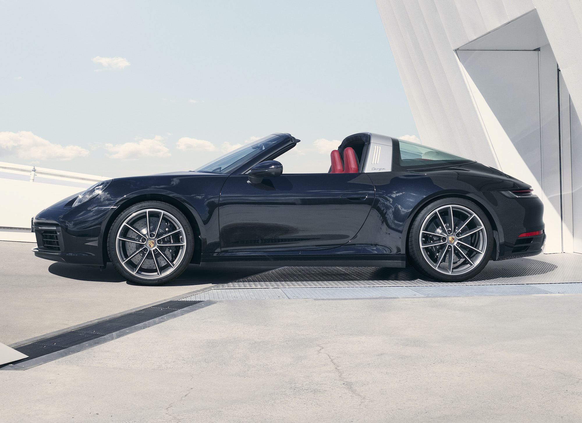 Najnowsza generacja Porsche 911 od teraz jest dostępna w swojej najbardziej transformersowej odmianie – Targa. Nie każdy może sobie pozwolić na zakup dwóch egzemplarzy Porsche 911. Z myślą o klientach, którzy chcieliby mieć zamknięte i otwarte 911, ale ich po prostu na nie nie stać, Porsche od 1965 r. produkuje model ze zdejmowaną centralną częścią dachu – Targa. Ten model jest jak dom w zabudowie szeregowej. Tak jak szeregówka łączy w sobie wszystkie wady mieszkania w bloku i wolno stojącego domu, tak w Tardze znajdziemy wady kabrioletu i wersji coupe. Z tego pierwszego mamy więc najwyższą masę własną spośród wszystkich wersji generacji 992 (1640 kg w Targa 4S z przekładnią manualną, 1675 kg 4S PDK) i mniejszą sztywność nadwozia kabrioletu, połączone z zamkniętą na stałe tylną częścią kabiny, która nie pozwala na pełne rozkoszowanie się wiatrem we włosach. Dobra, starczy tych zgryźliwości. Tak jak wielu dostrzega mnóstwo zalet w zabudowie szeregowej, tak samo wielu może zachwycać się tą najbardziej niezwykłą wizualnie odmianą 911. Dla tych, którzy wykorzystują to auto wyłącznie do relaksacyjnych podróży i nie szukają limitów przyczepności na torze, Targa może być najbardziej uniwersalną i wszechstronnie utalentowaną odmianą 911, która na przemianę z coupe w prawie-kabriolet potrzebuje zaledwie 19 s (7 s więcej niż w wersji cabrio). A robi to tak: I wygląda na to, że klientom się to podoba, bo na Targę decyduje się 18 proc. klientów kupujących 911. Od pasa w dół – jak zwykłe 911. To oznacza, że poza fikuśnym dachem odmiana Targa nie różni się od podstawowego 4 i 4S. Zasilana jest trzylitrowym, sześciocylindrowym boxerem o mocy 380 (4) lub 444 (4S) KM. Ten słabszy ma 450 Nm momentu obrotowego, mocniejszy – 530 Nm. 4 rozpędza się do 100 km/h 2 4,4 s i kończy przyspieszać po osiągnięciu 289 km/h, a 4S z PDK na sprint do setki potrzebuje 3,6 s i nie pojedzie szybciej niż 304 km/h. Zaznaczam, że z PDK, bo z siedmiobiegową przekładnią manualną, którą można zamówić do tej wersji przyspieszenie do 100 km/h wprawnemu kierowcy zajmuje co najmniej 4,4 s, czyli tyle, co byle jakiemu w Tardze 4. Targa dostępna jest wyłącznie z napędem na cztery koła. Nic nie zapowiada, by miała pojawić się odmiana z napędem na tylną oś. Według Franka-Steffena Wallisera, szefa działu samochodów sportowych w Porsche, nie ma też szans na to, by np. odmiany Targa doczekała się 911-ka Turbo. Cenę auta poznamy pewnie za chwilę, a pierwsze egzemplarze mają trafić do klientów jeszcze pod koniec tego roku. 
