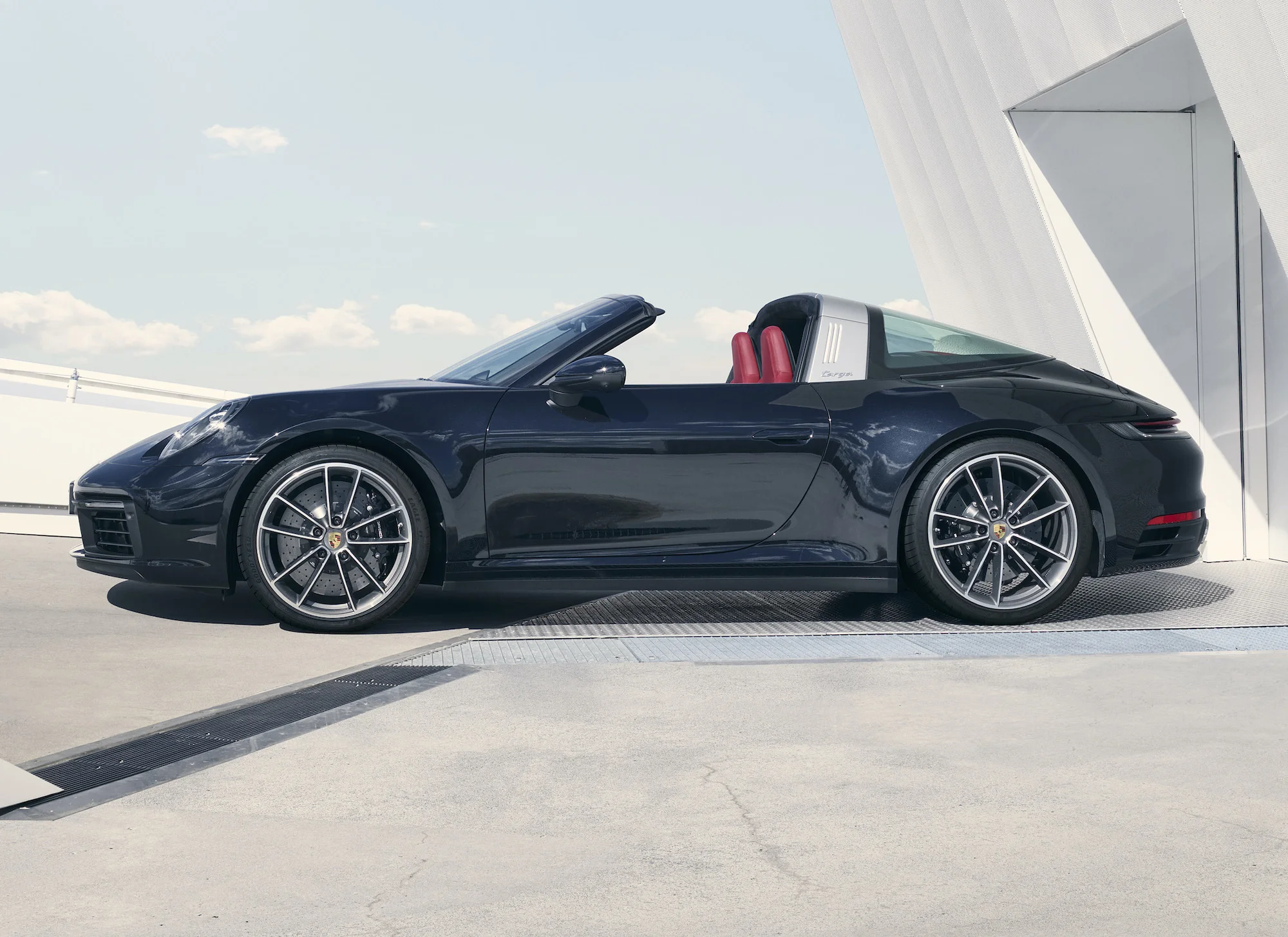 Najnowsza generacja Porsche 911 od teraz jest dostępna w swojej najbardziej transformersowej odmianie – Targa. Nie każdy może sobie pozwolić na zakup dwóch egzemplarzy Porsche 911. Z myślą o klientach, którzy chcieliby mieć zamknięte i otwarte 911, ale ich po prostu na nie nie stać, Porsche od 1965 r. produkuje model ze zdejmowaną centralną częścią dachu – Targa. Ten model jest jak dom w zabudowie szeregowej. Tak jak szeregówka łączy w sobie wszystkie wady mieszkania w bloku i wolno stojącego domu, tak w Tardze znajdziemy wady kabrioletu i wersji coupe. Z tego pierwszego mamy więc najwyższą masę własną spośród wszystkich wersji generacji 992 (1640 kg w Targa 4S z przekładnią manualną, 1675 kg 4S PDK) i mniejszą sztywność nadwozia kabrioletu, połączone z zamkniętą na stałe tylną częścią kabiny, która nie pozwala na pełne rozkoszowanie się wiatrem we włosach. Dobra, starczy tych zgryźliwości. Tak jak wielu dostrzega mnóstwo zalet w zabudowie szeregowej, tak samo wielu może zachwycać się tą najbardziej niezwykłą wizualnie odmianą 911. Dla tych, którzy wykorzystują to auto wyłącznie do relaksacyjnych podróży i nie szukają limitów przyczepności na torze, Targa może być najbardziej uniwersalną i wszechstronnie utalentowaną odmianą 911, która na przemianę z coupe w prawie-kabriolet potrzebuje zaledwie 19 s (7 s więcej niż w wersji cabrio). A robi to tak: I wygląda na to, że klientom się to podoba, bo na Targę decyduje się 18 proc. klientów kupujących 911. Od pasa w dół – jak zwykłe 911. To oznacza, że poza fikuśnym dachem odmiana Targa nie różni się od podstawowego 4 i 4S. Zasilana jest trzylitrowym, sześciocylindrowym boxerem o mocy 380 (4) lub 444 (4S) KM. Ten słabszy ma 450 Nm momentu obrotowego, mocniejszy – 530 Nm. 4 rozpędza się do 100 km/h 2 4,4 s i kończy przyspieszać po osiągnięciu 289 km/h, a 4S z PDK na sprint do setki potrzebuje 3,6 s i nie pojedzie szybciej niż 304 km/h. Zaznaczam, że z PDK, bo z siedmiobiegową przekładnią manualną, którą można zamówić do tej wersji przyspieszenie do 100 km/h wprawnemu kierowcy zajmuje co najmniej 4,4 s, czyli tyle, co byle jakiemu w Tardze 4. Targa dostępna jest wyłącznie z napędem na cztery koła. Nic nie zapowiada, by miała pojawić się odmiana z napędem na tylną oś. Według Franka-Steffena Wallisera, szefa działu samochodów sportowych w Porsche, nie ma też szans na to, by np. odmiany Targa doczekała się 911-ka Turbo. Cenę auta poznamy pewnie za chwilę, a pierwsze egzemplarze mają trafić do klientów jeszcze pod koniec tego roku.